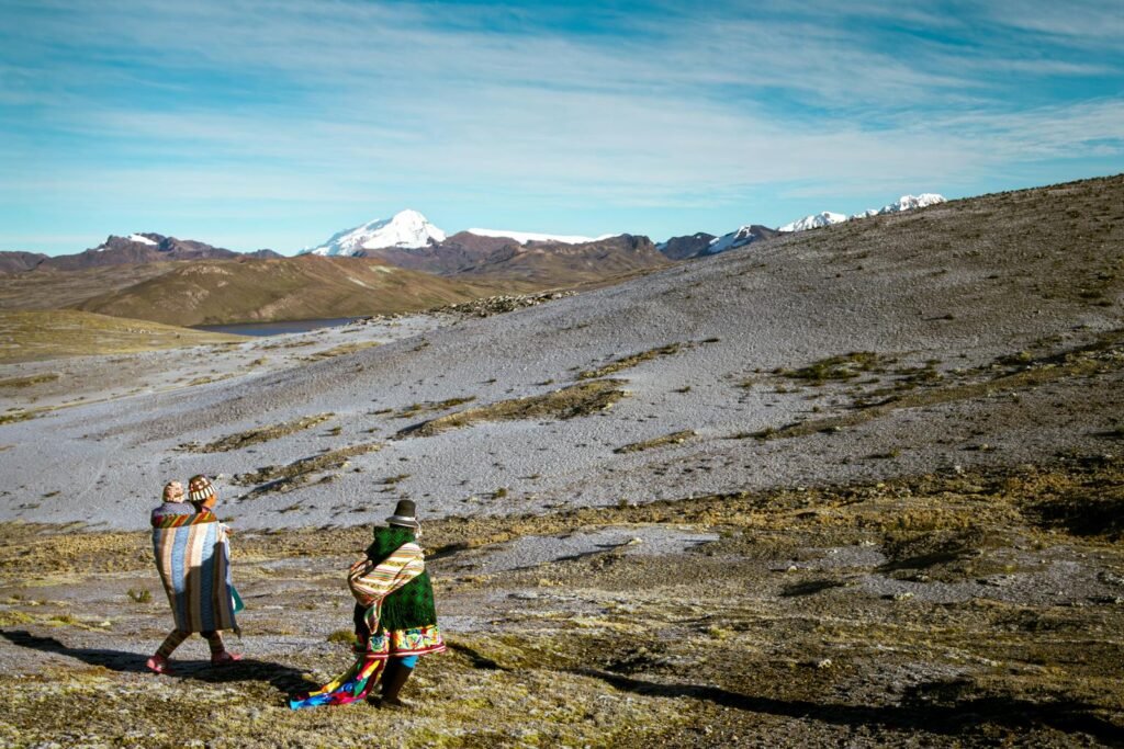 Two people wrapped in blankets walking in the Peruvian Andes with mountains in the distance.